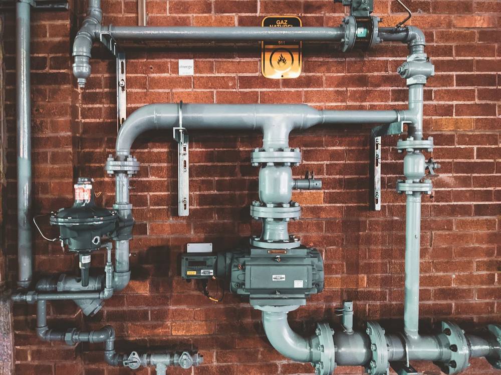 A service setting of pipes, valves and a register on a brick wall